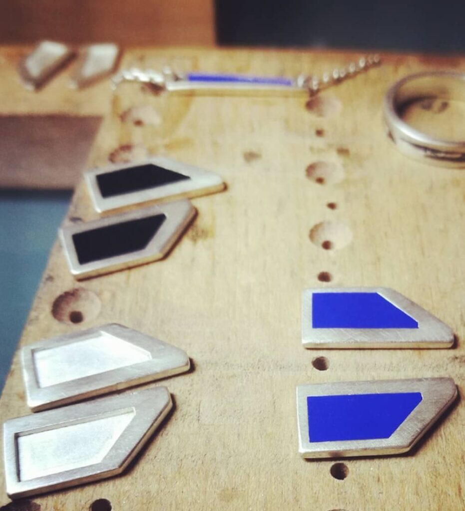 Sélection de bijoux Auclair-Création (bagues, bracelets) sur support en bois, en attente ou après application de la laque biosourcée, témoignant du processus de finition en atelier.